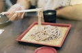 Hand of woman use chopsticks to clamp a noodle on a bamboo dish, japanese noodle, itÃ¢â¬â¢s call Soba, selective focus at noodle Royalty Free Stock Photo